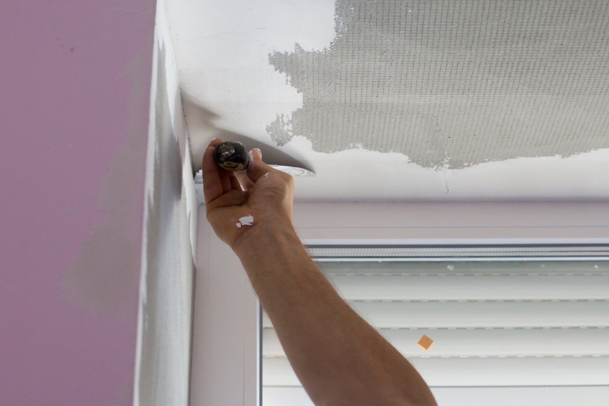 Hand holding a tool performing skim coat on ceiling.