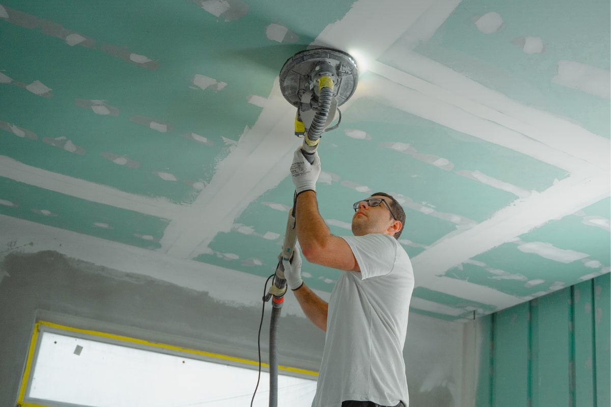 Worker applying plaster and making ceiling repairs with a handheld surfacing device.