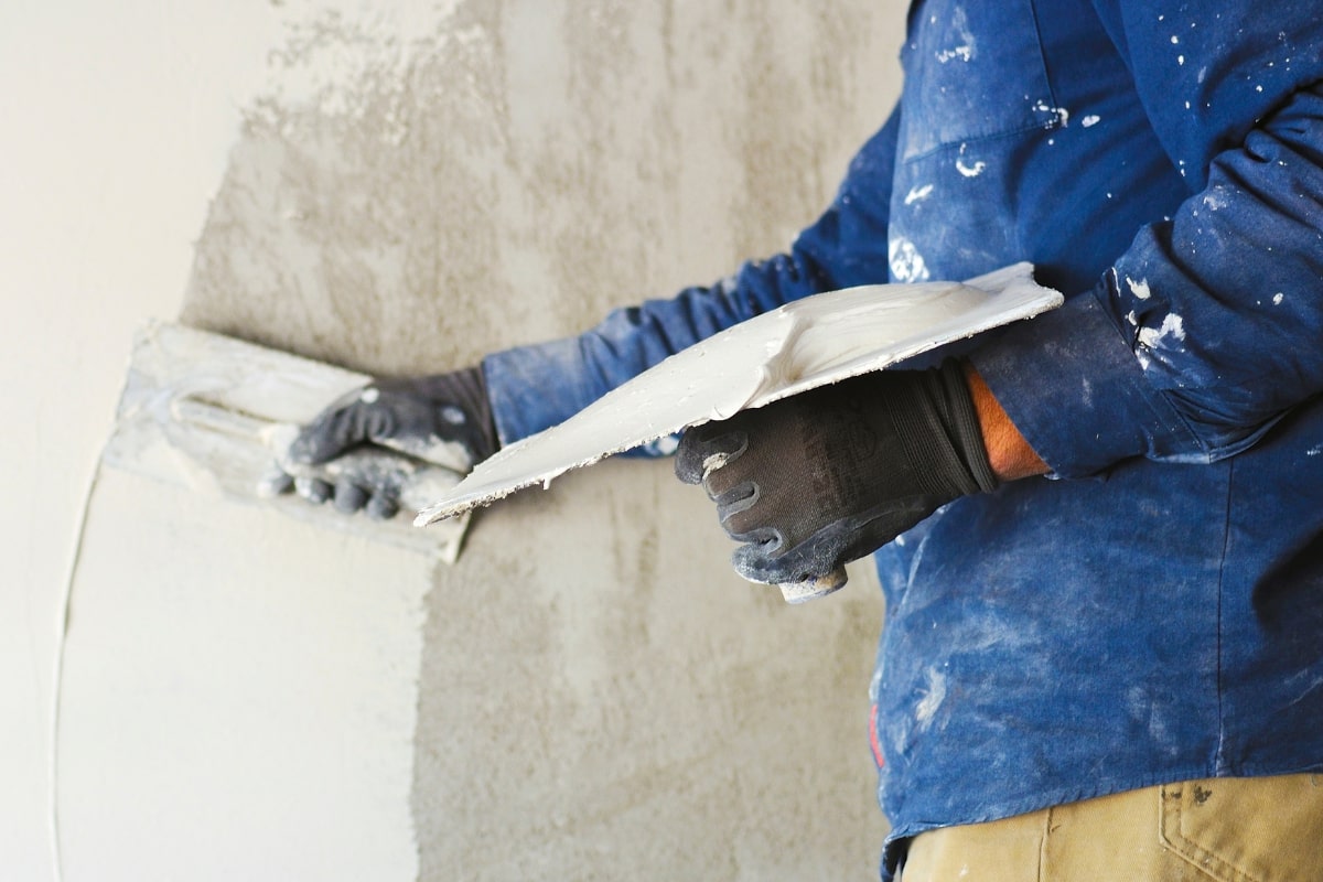 Man applying plaster to a wall using construction tools for solid plastering, stucco, and sponge finish.