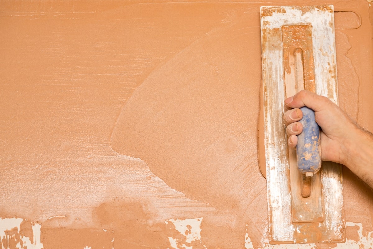 Close-up of a hand spreading coloured plaster on a wall with a smoothing device.